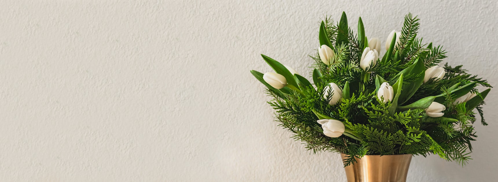 Elegant white tulips nestled among lush greenery in a stylish vase, perfect for any occasion.