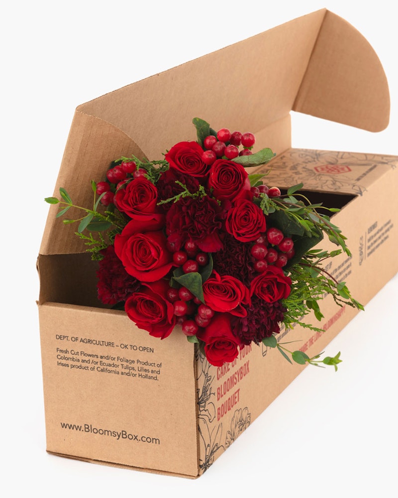 Cardboard box with a beautiful bouquet of red roses and green foliage spilling out, displayed against a clean, white background, perfect for a romantic gesture.