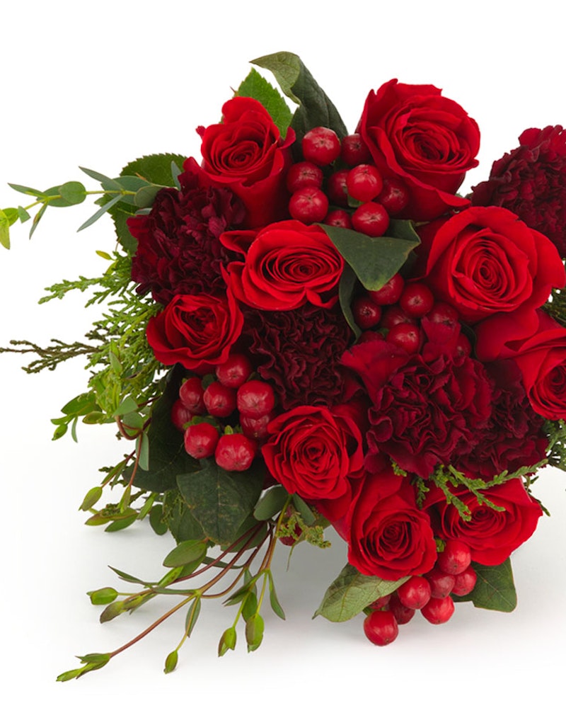 Lush bouquet of deep red roses, carnations, berries, and greenery against a white background, creating a luxurious and romantic floral arrangement.