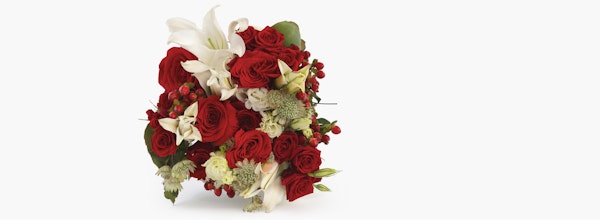 Elegant bouquet featuring vibrant red roses, white lilies, and greenery with hints of small red berries, arranged artistically on a neutral background.