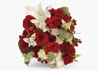 Elegant bouquet featuring vibrant red roses, white lilies, and greenery with hints of small red berries, arranged artistically on a neutral background.