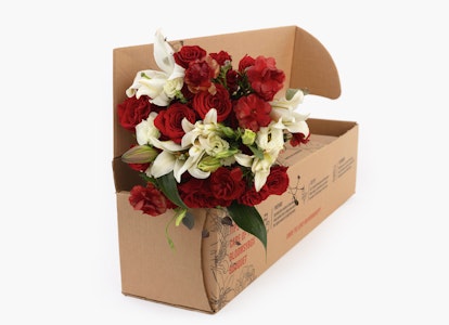 Open cardboard box with a fresh bouquet of red roses and white lilies on a white background, representing online flower delivery service.