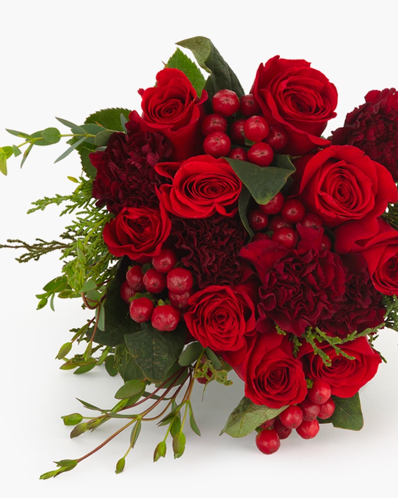 Elegant bouquet of deep red roses, carnations, and berry sprigs with lush green leaves against a clean white background perfect for romantic occasions.