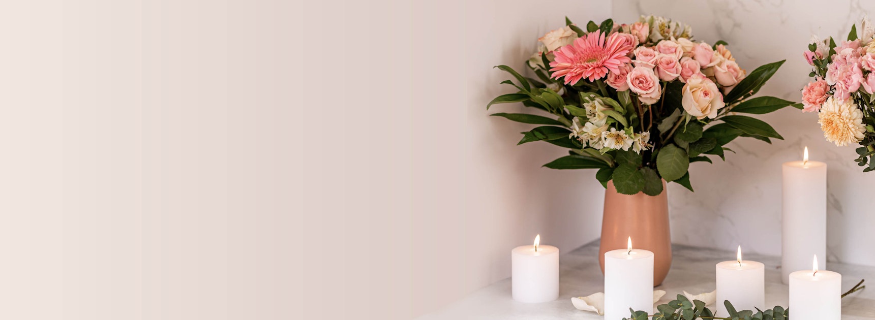 Elegant floral arrangement featuring pink gerbera daisies and roses, accompanied by lit candles.