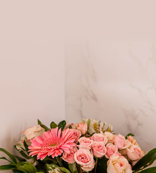 A lovely arrangement of pink gerbera daisies and soft pink roses against a neutral backdrop.