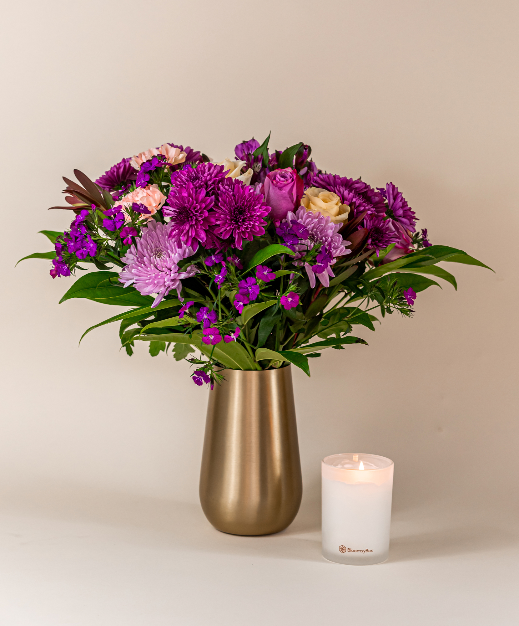 Elegant floral arrangement featuring purple and pink blooms alongside a chic candle.