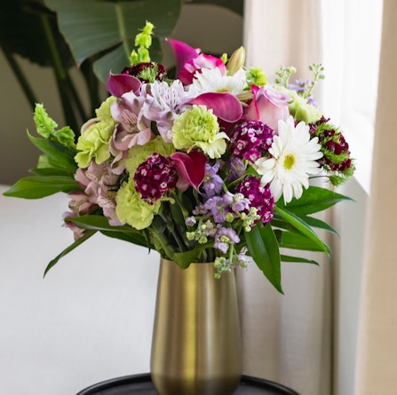 Vibrant floral arrangement featuring purple, green, and white flowers in a modern vase.