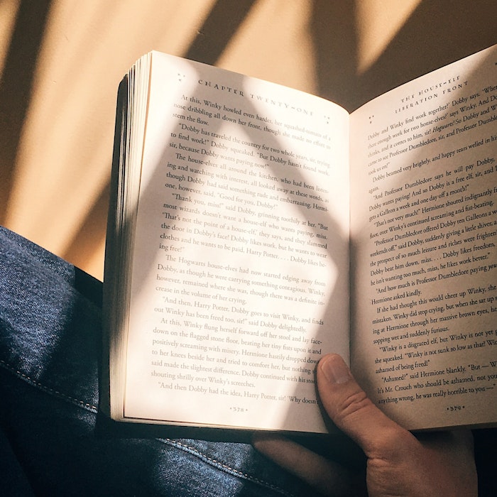 Person sitting and reading a book with pages illuminated by warm sunlight casting shadows, suggesting a peaceful and relaxed reading atmosphere.