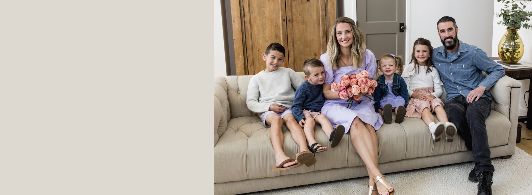 A joyful family portrait on a cozy couch, featuring a woman with a bouquet of pink roses.