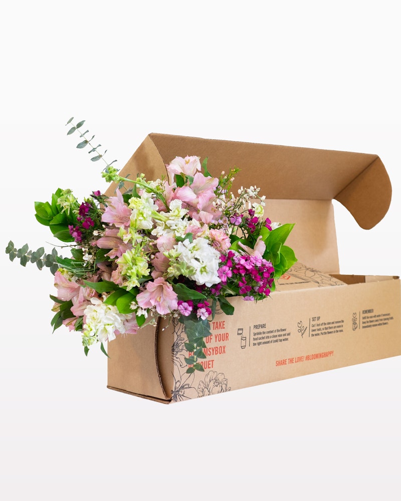 A vibrant bouquet of pink and white flowers with greenery arranged in an open cardboard box, designed for an elegant and eco-friendly presentation.