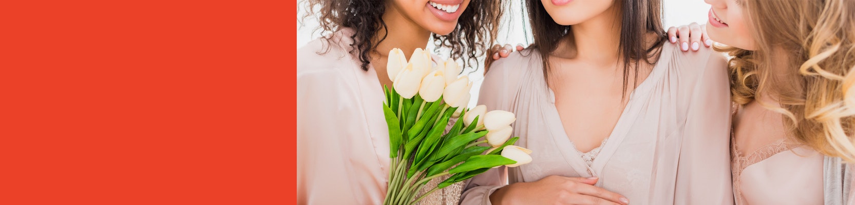 Three smiling women in soft attire, holding a bouquet of fresh tulips, celebrating friendship.