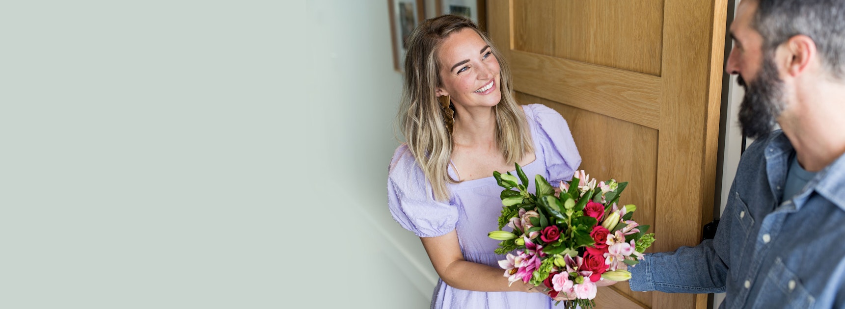 A joyful woman in a purple dress receives a colorful flower bouquet at home.