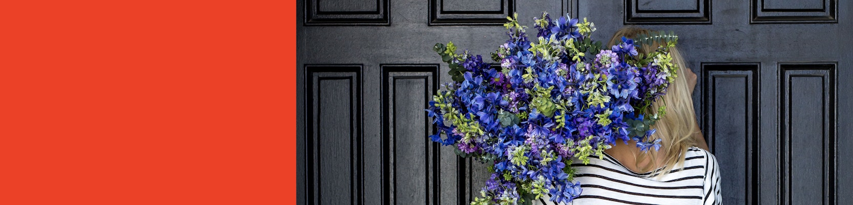 A woman holding a vibrant bouquet of blue and green flowers against a stylish door.