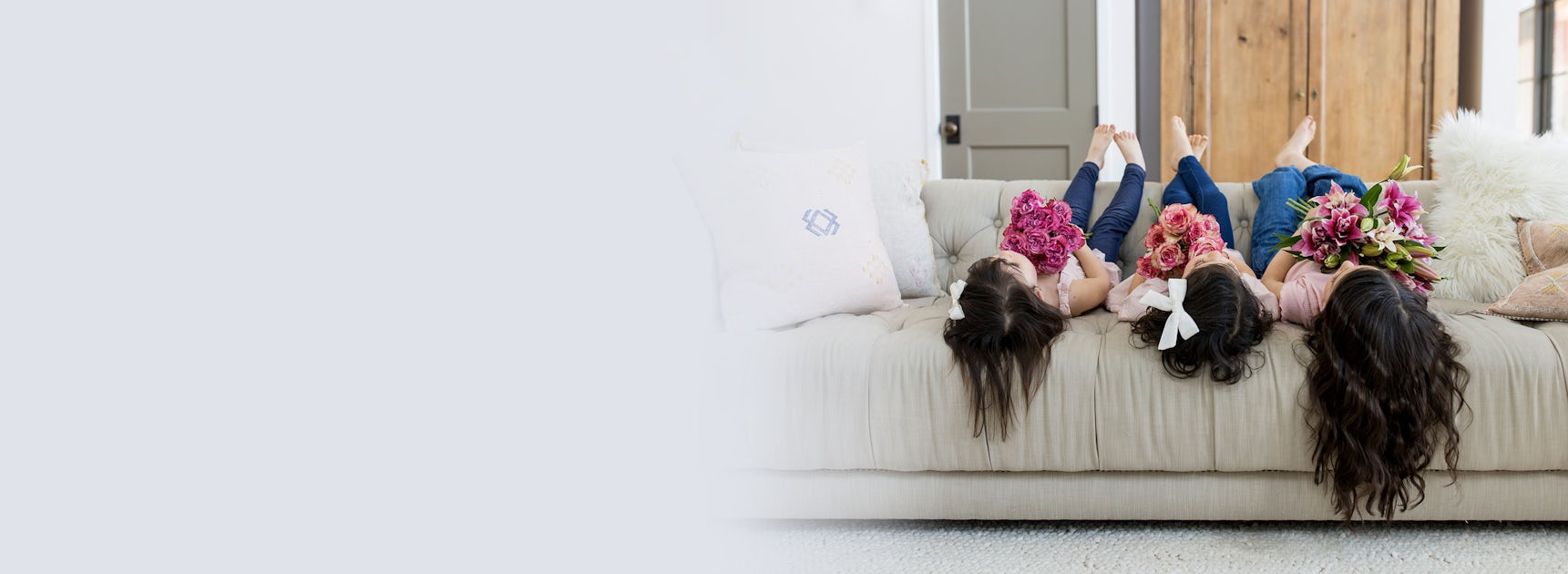Three girls lounging on a cozy sofa, joyfully holding vibrant floral bouquets.