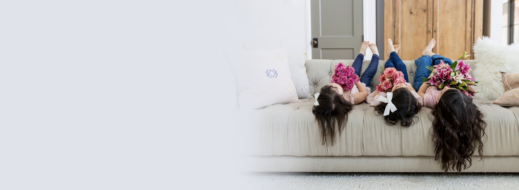 Three girls lounging on a cozy sofa, joyfully holding vibrant floral bouquets.