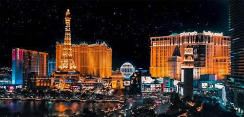 Vibrant night view of the Las Vegas Strip featuring the illuminated replicas of the Eiffel Tower and Paris Balloon, with the Planet Hollywood Resort.