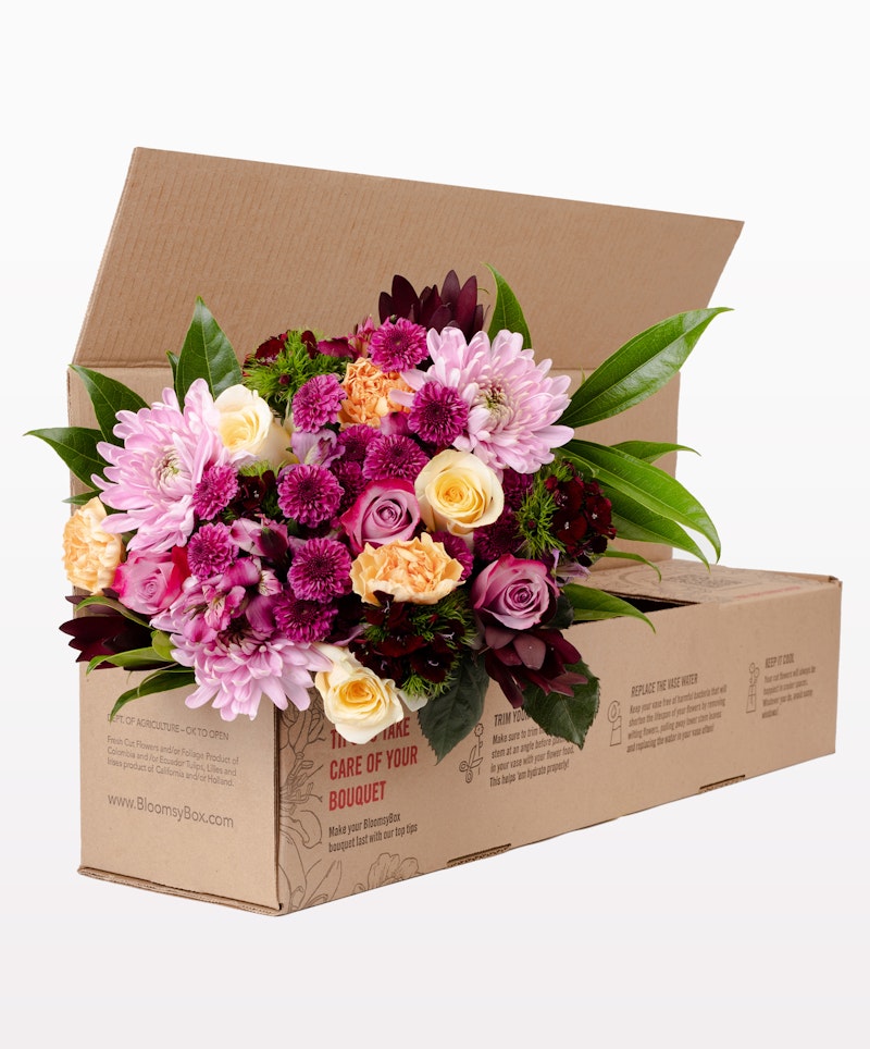 Fresh bouquet of pink and cream roses, chrysanthemums, and other flowers packaged neatly in a brown cardboard box with care instructions for optimal SEO.