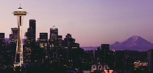 Seattle skyline at dusk featuring the iconic Space Needle with Mount Rainier in the background under a purple sky, showcasing urban beauty and nature.