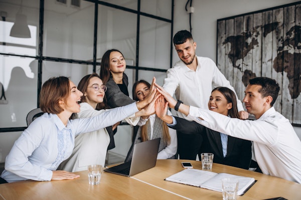 A diverse team of professionals celebrating teamwork with high-fives in a modern office setting.