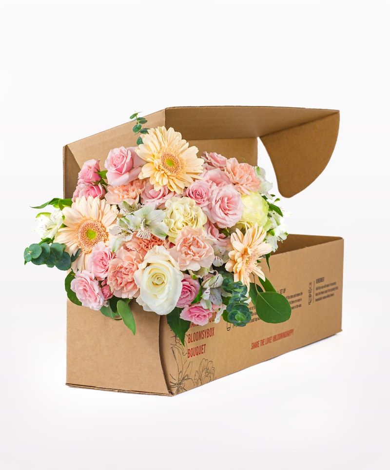 A vibrant bouquet of pink roses, white flowers, and yellow blooms spilling out of a cardboard box on a white background, showcasing a fresh flower delivery concept.