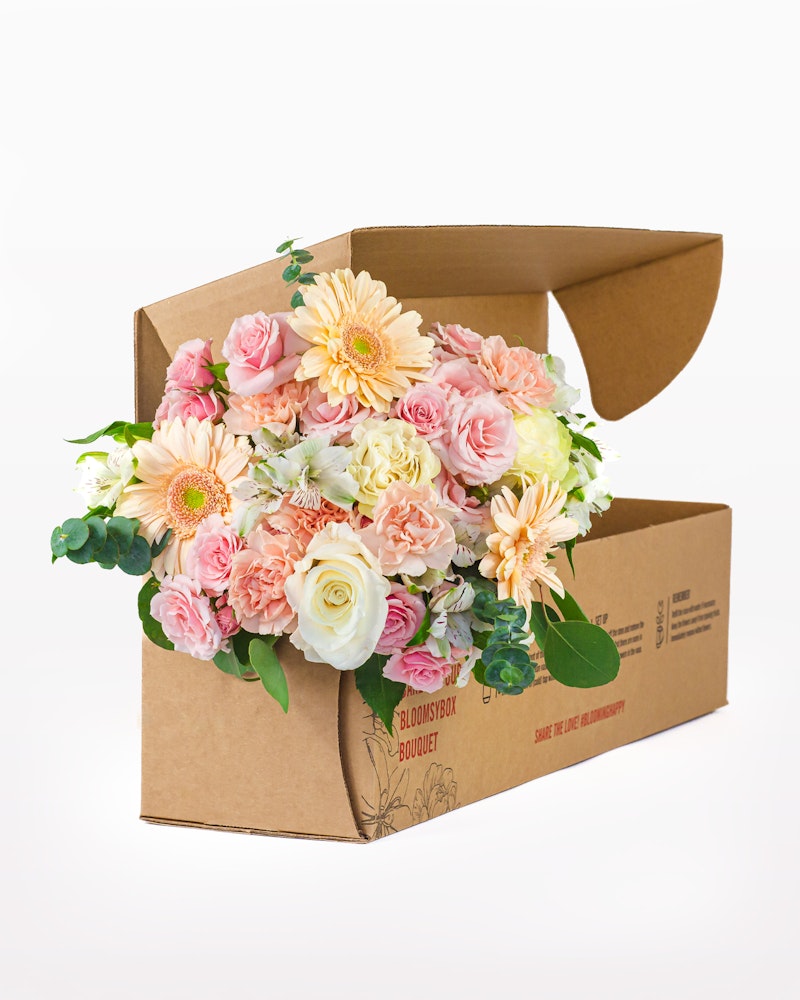 A vibrant bouquet of pink roses, white flowers, and yellow blooms spilling out of a cardboard box on a white background, showcasing a fresh flower delivery concept.