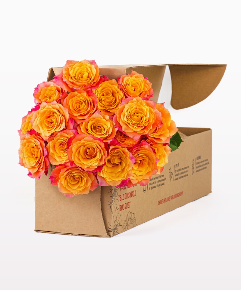 Bright orange and pink roses arranged tastefully in an open brown cardboard box with a "joyfully fresh bouquet" label, set against a clean white background.