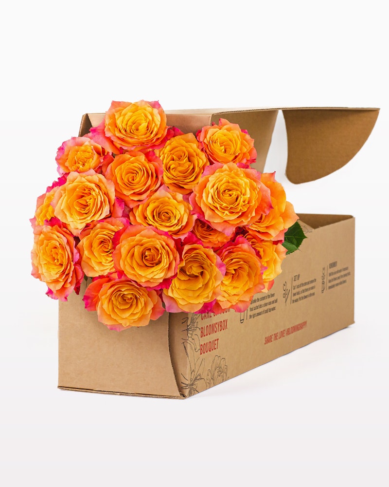 Bright orange and pink roses arranged tastefully in an open brown cardboard box with a "joyfully fresh bouquet" label, set against a clean white background.
