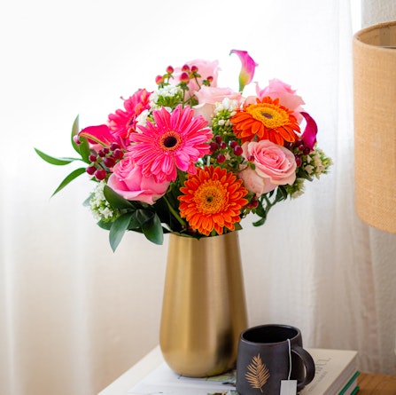 Bright and vibrant floral arrangement featuring pink gerbera daisies, roses, and orange blooms.