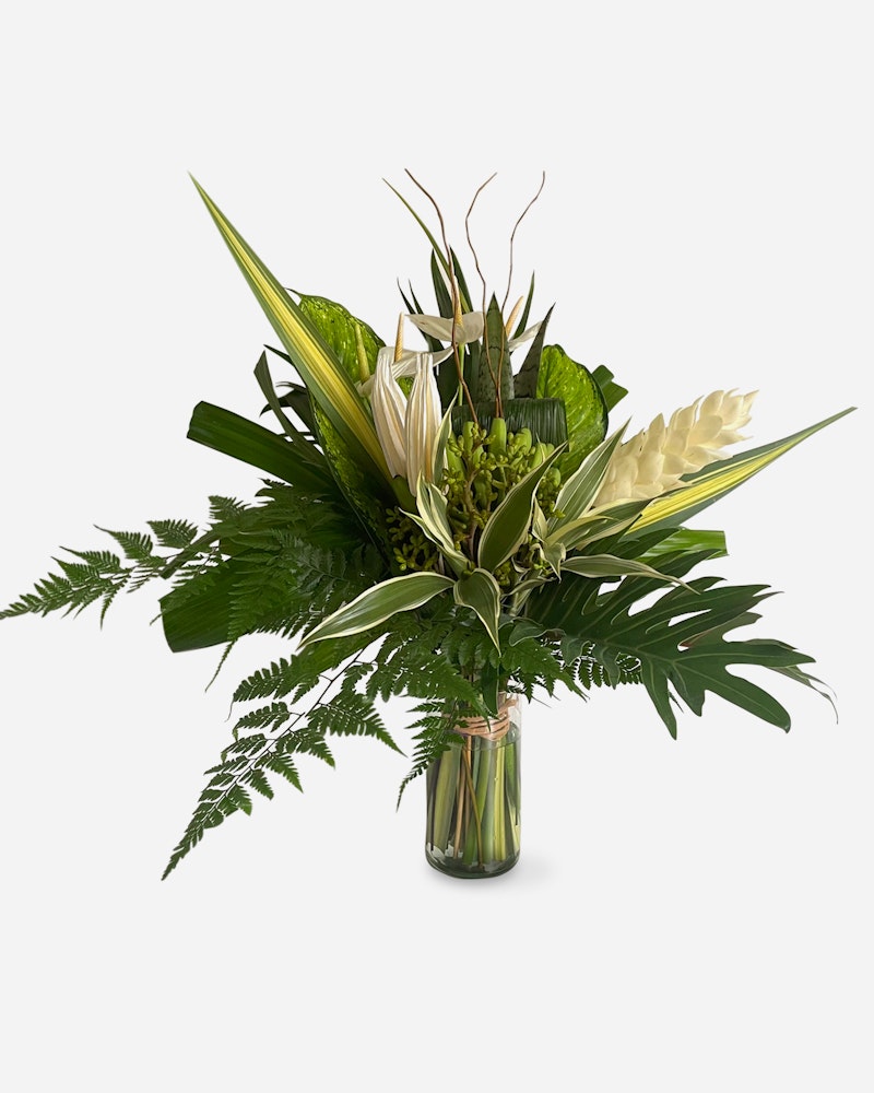 Elegant bouquet of white lilies, tropical leaves, and ferns arranged in a clear glass vase against a plain white background, perfect for sophisticated decor.