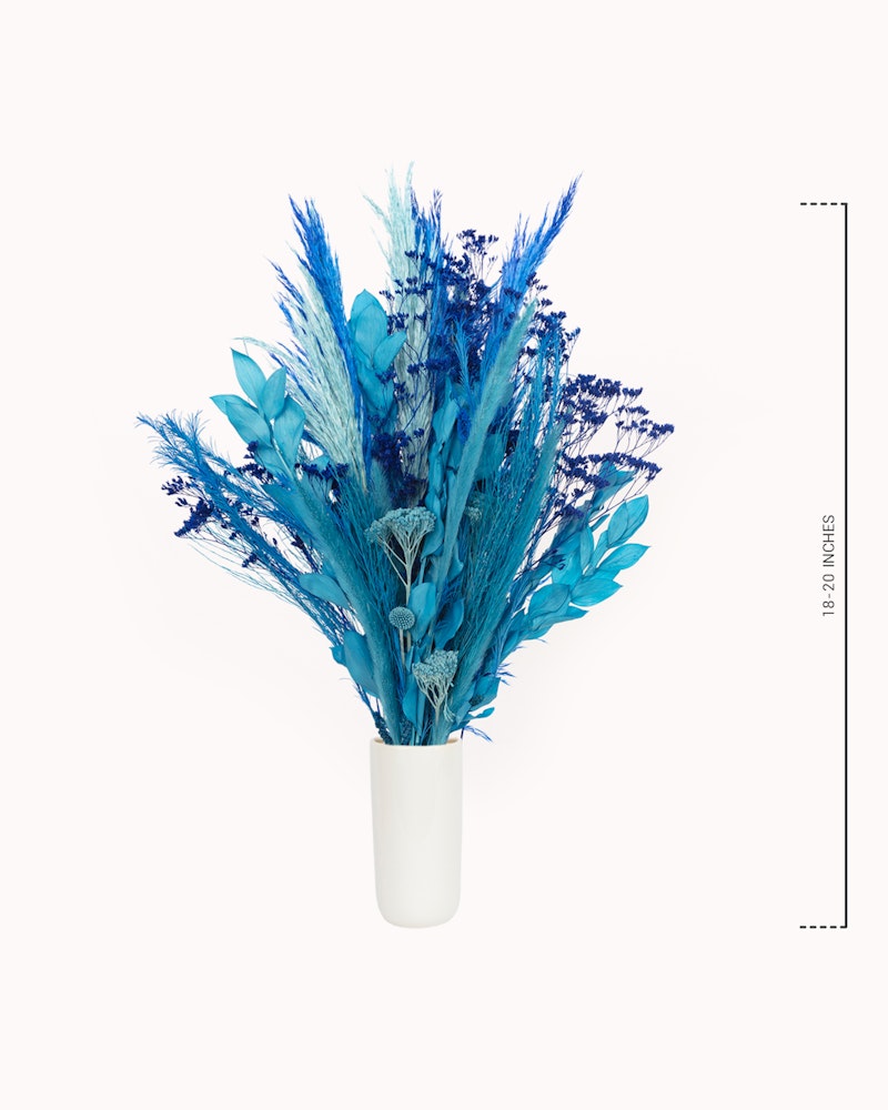 Blue dyed pampas grass and botanicals arranged in a modern white vase, isolated on a white background, with a measurement scale to the right.