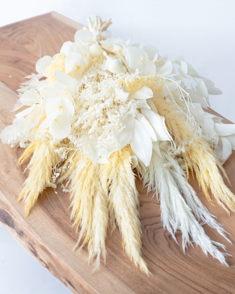 A decorative floral arrangement with white petals and yellow accents artfully displayed on a natural wooden board, ideal for weddings or elegant events.