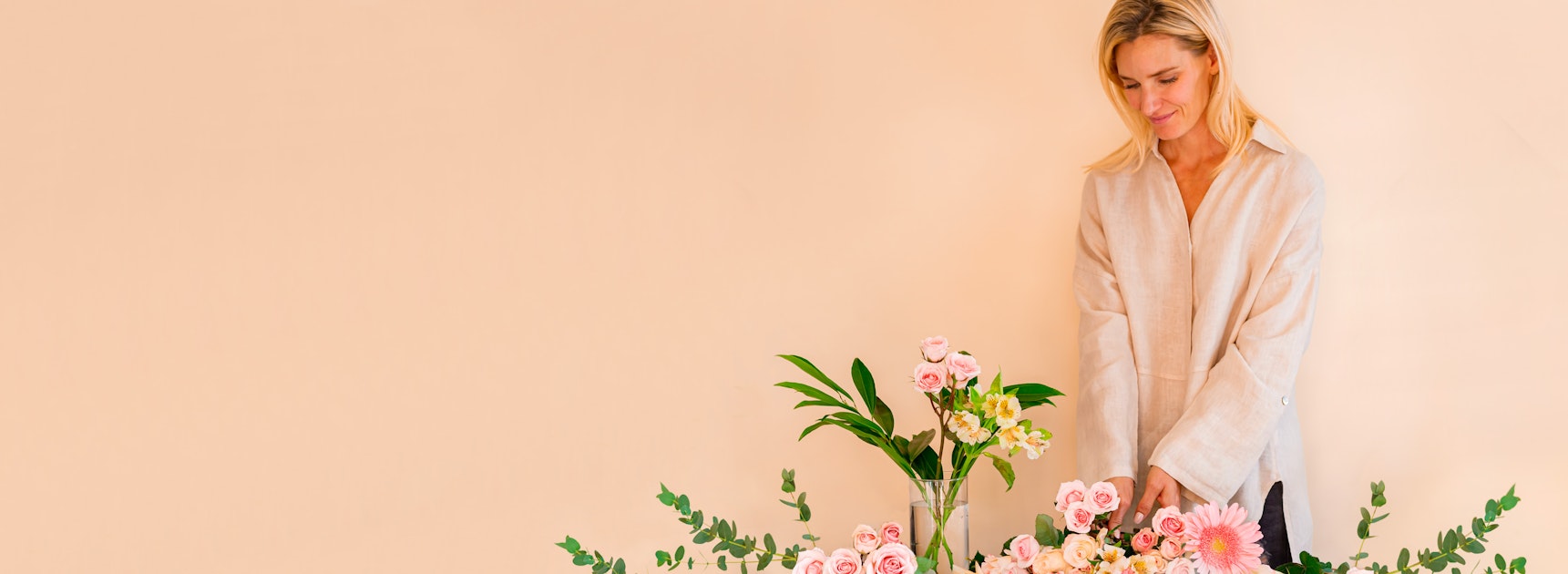 A woman arranging a vibrant floral display with pink and yellow blooms against a warm background.
