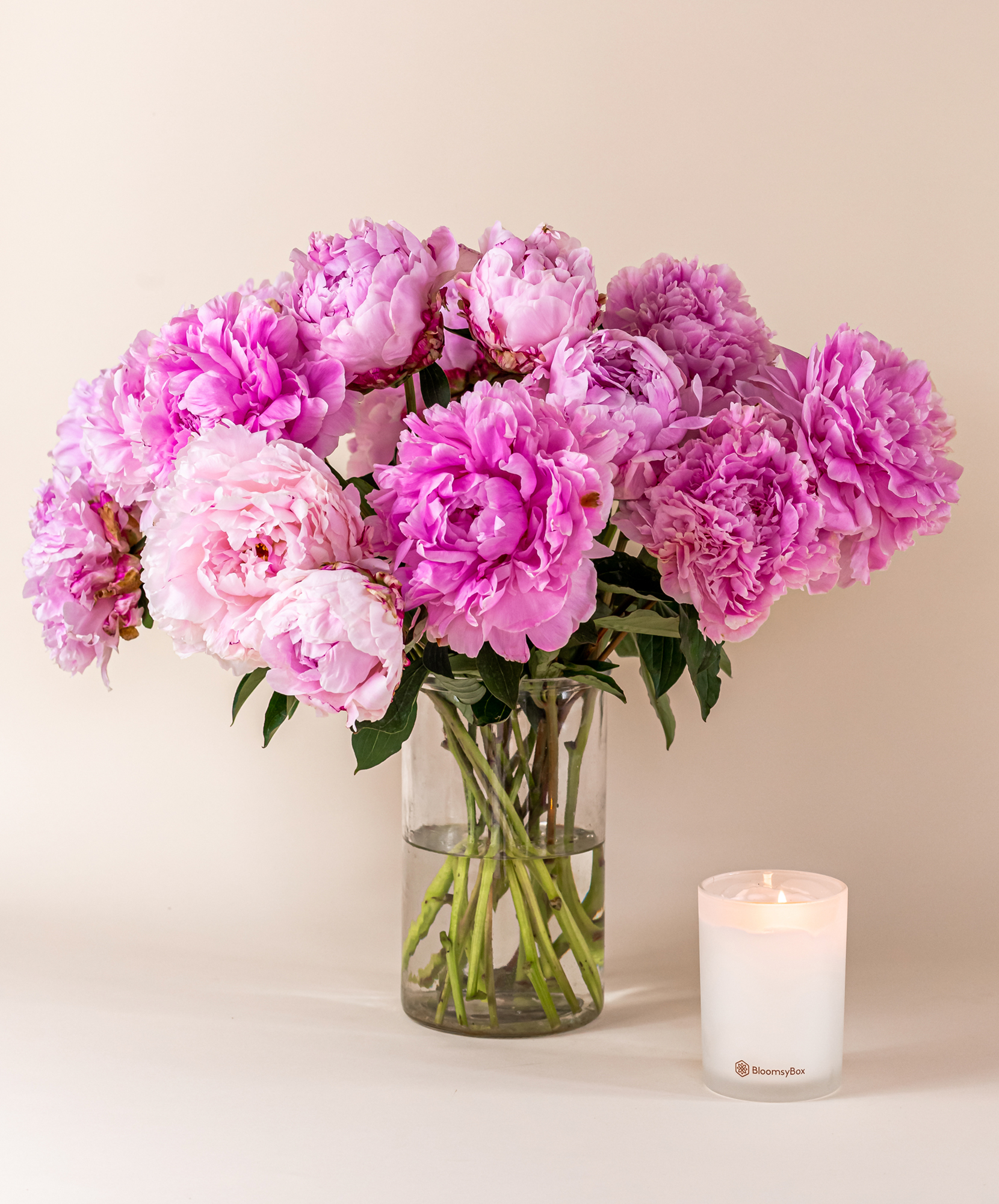 A gentle arrangement of pink peonies in a glass vase, paired with a lit candle.