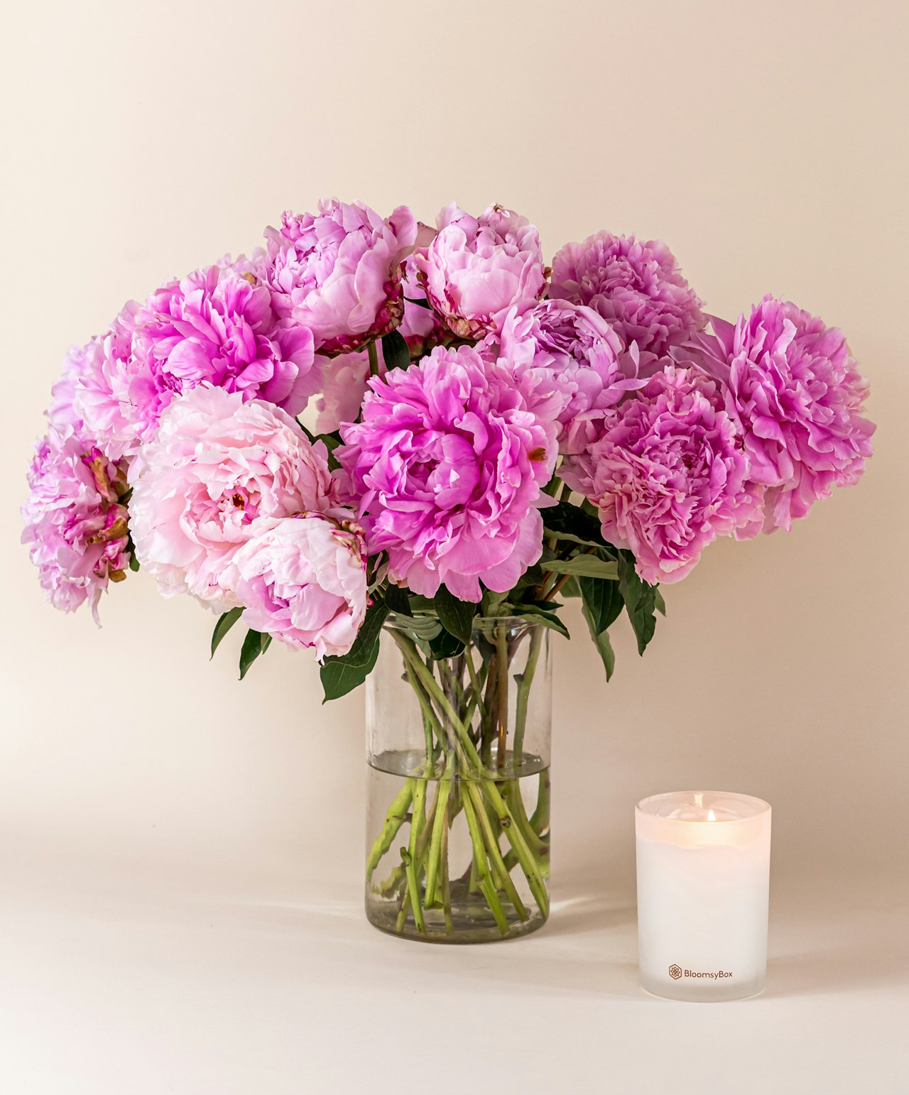 A gentle arrangement of pink peonies in a glass vase, paired with a lit candle.