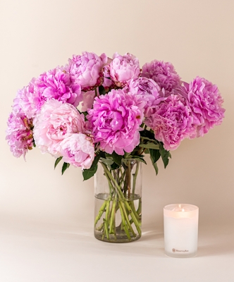 A gentle arrangement of pink peonies in a glass vase, paired with a lit candle.
