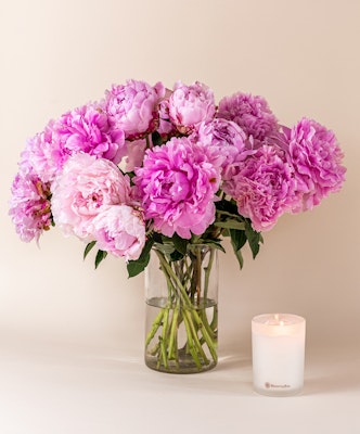A gentle arrangement of pink peonies in a glass vase, paired with a lit candle.