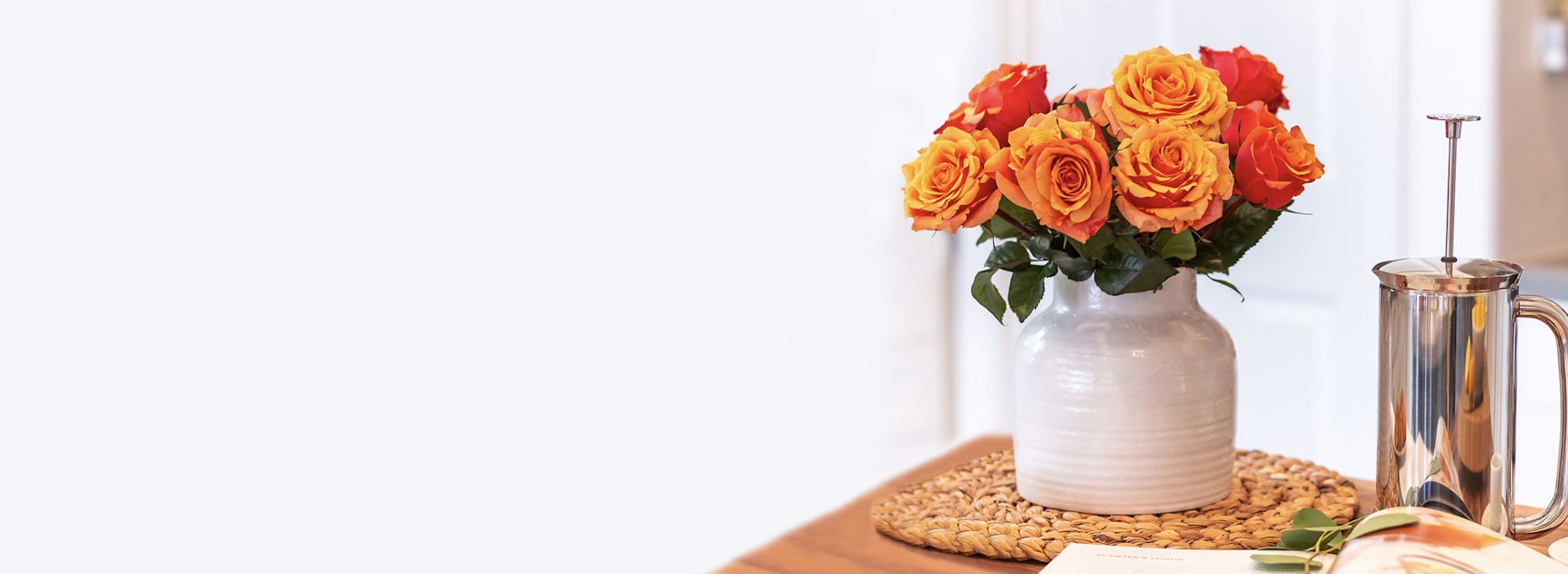 Vibrant bouquet of orange and yellow roses in a stylish vase on a wooden table.