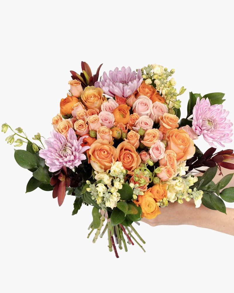 Two hands holding a vibrant bouquet of flowers featuring roses, chrysanthemums, and assorted foliage against a white background.