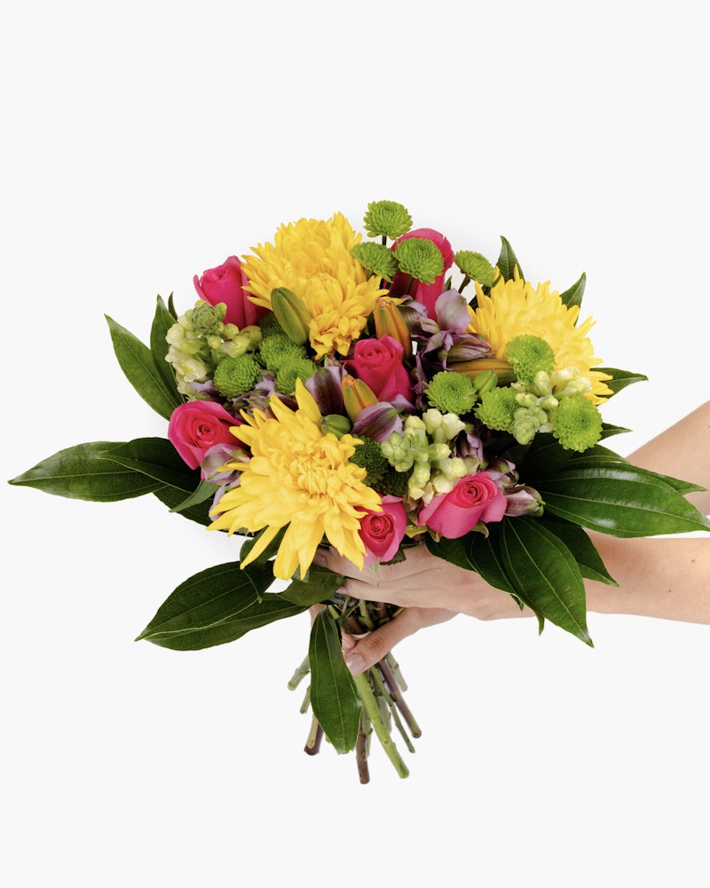 A person holding a vibrant bouquet of flowers including yellow chrysanthemums, pink roses, and greenery, isolated on a white background.