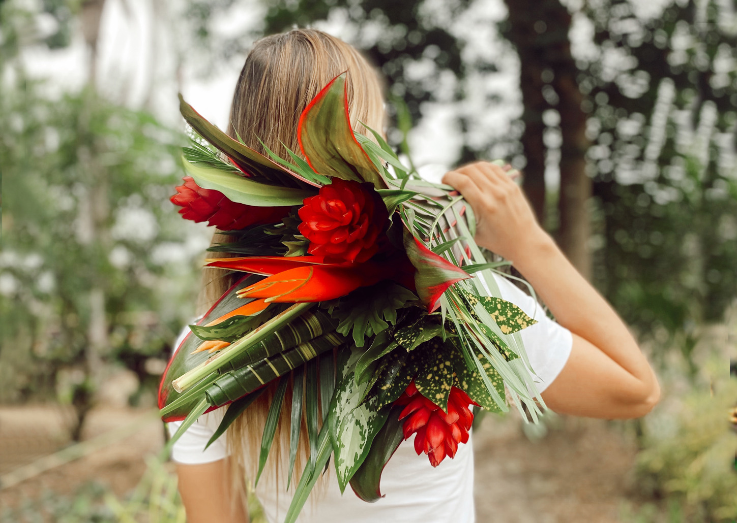 A woman holding a vibrant tropical flower bouquet against a lush green backdrop.