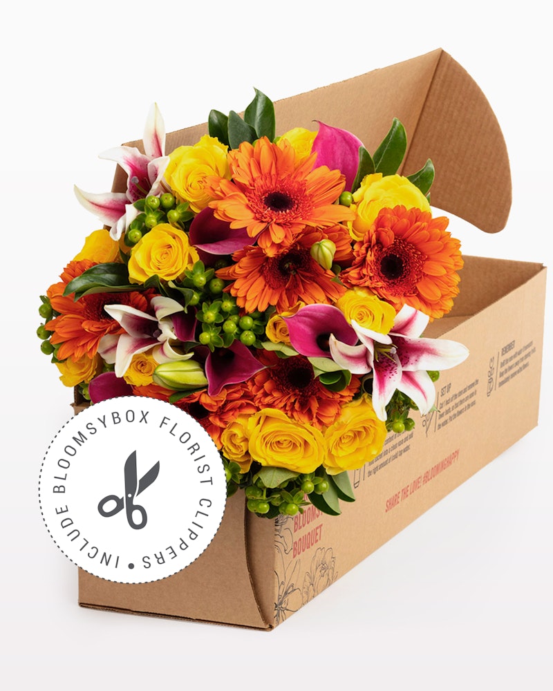 Vibrant bouquet of fresh flowers with orange gerberas, pink lilies, and yellow roses packaged in a BloomsyBox, a branded cardboard flower box.