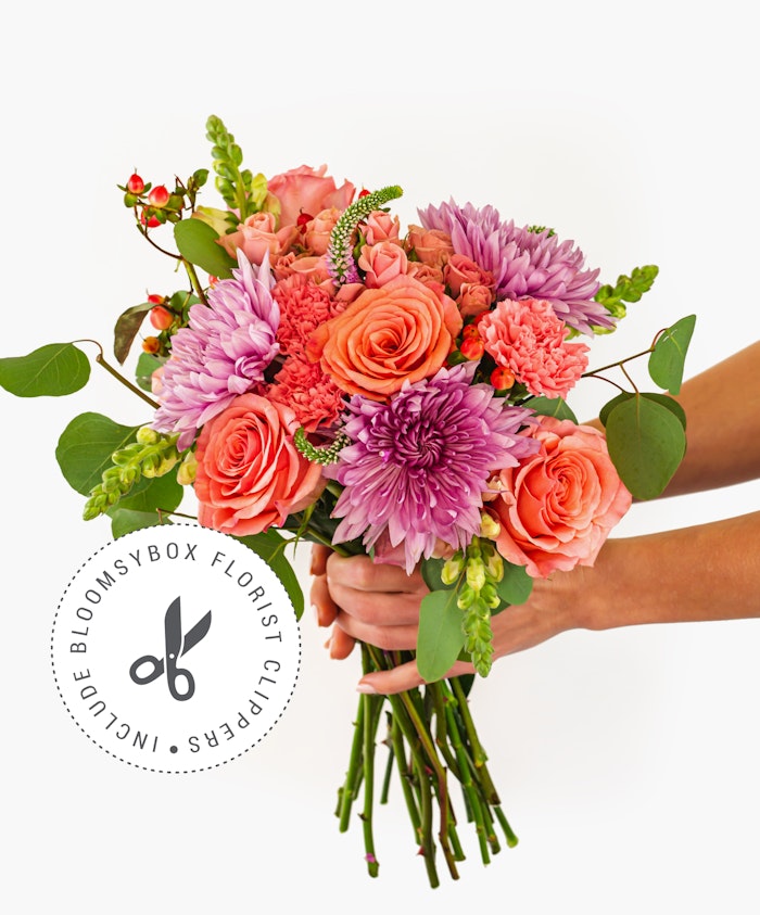 Vibrant floral bouquet featuring coral roses, purple chrysanthemums, and delicate greens.