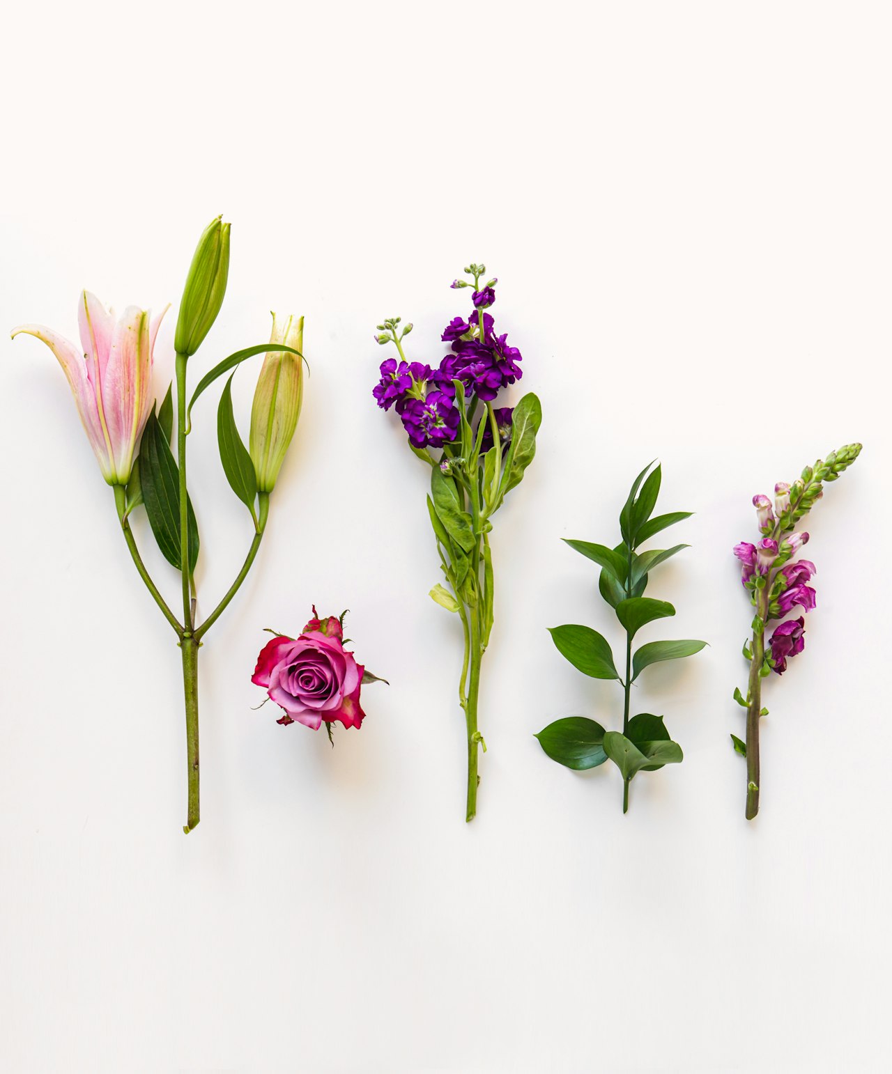 A colorful display of flowers including lilies, roses, and purple blooms on a white background.