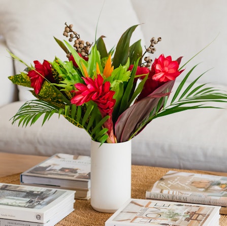Vibrant tropical flower arrangement with red blooms and lush greenery in a stylish vase.