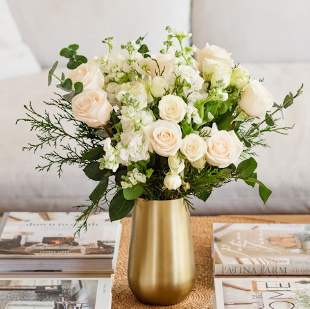 Elegant bouquet of white roses and greenery in a gold vase, perfect for home décor.