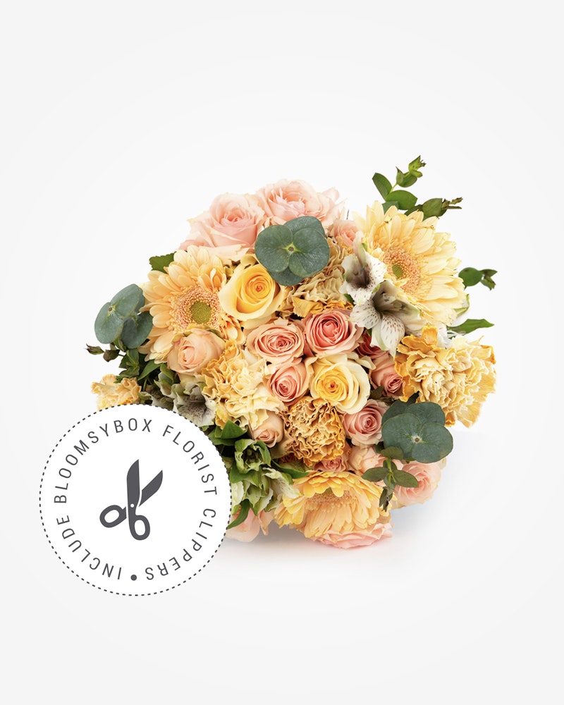 A vibrant bouquet of assorted flowers including yellow roses, peach carnations, and greenery against a white backdrop with the logo "BloomsyBox Florist Collective."