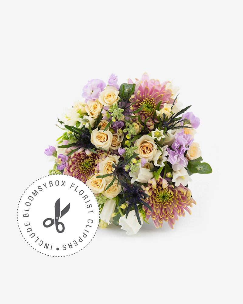A vibrant bouquet of mixed flowers including purple roses, white lilies, and assorted greenery, by BloomsyBox Florist displayed on a white background.