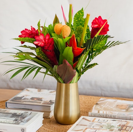 Vibrant tropical flower arrangement featuring red and orange blooms in a stylish vase.