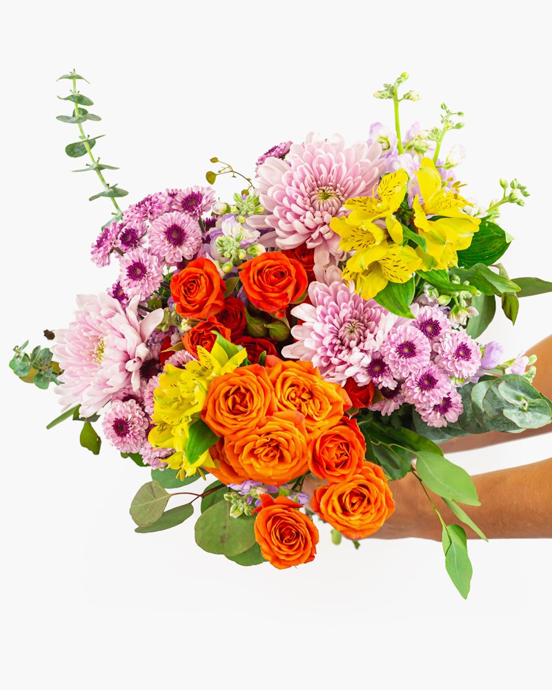 Vibrant bouquet of flowers including orange roses, pink chrysanthemums, and yellow lilies held in hand against a white background, perfect for special occasions.