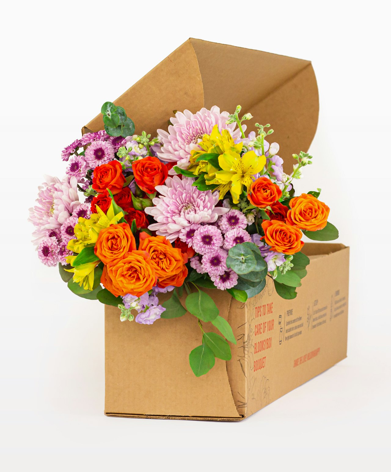 Vibrant floral arrangement featuring orange roses, colorful chrysanthemums, and greenery in a box.